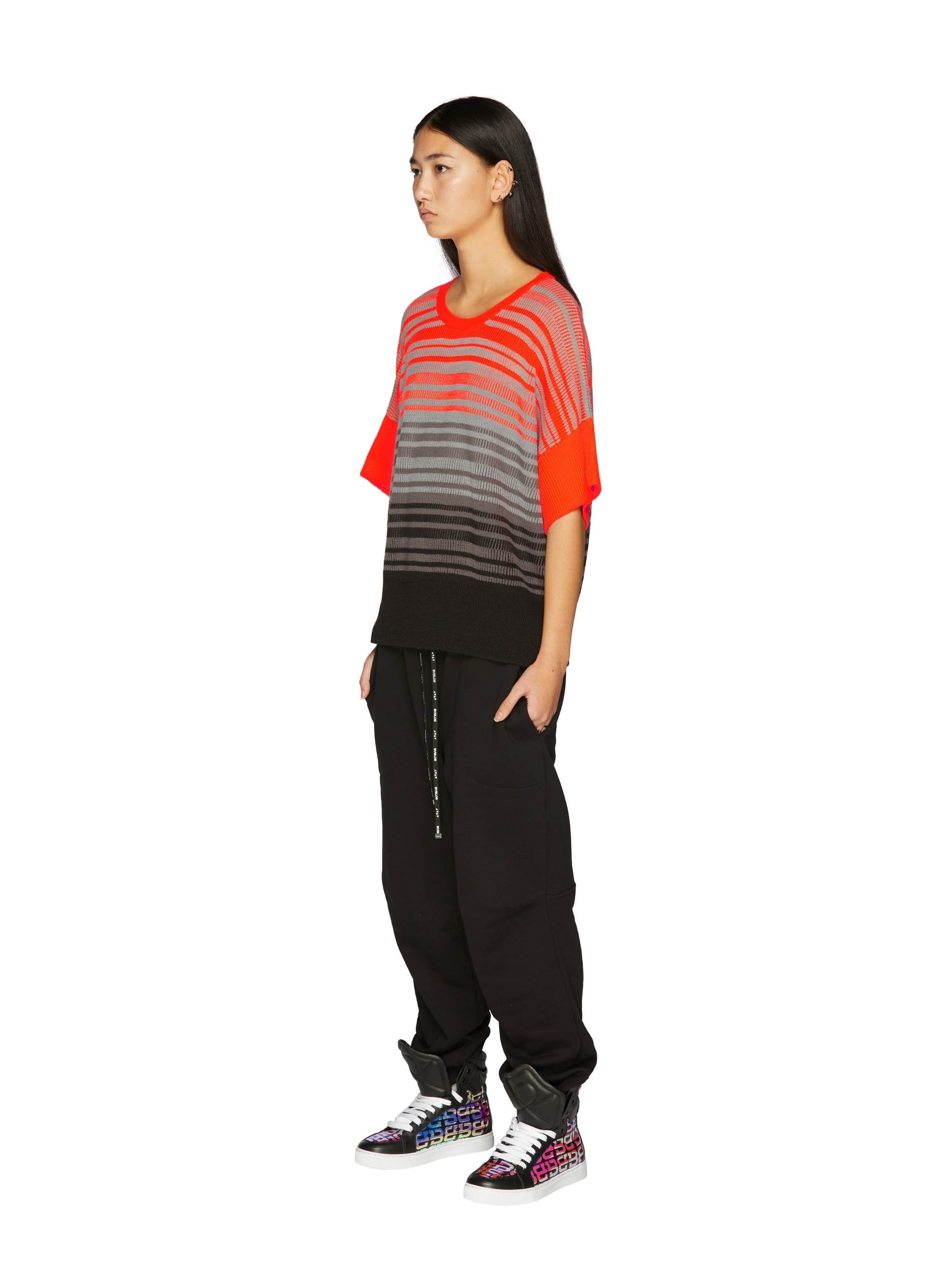Model wearing a striped oversized knit top in red and gray, paired with black joggers and colorful high-top sneakers.