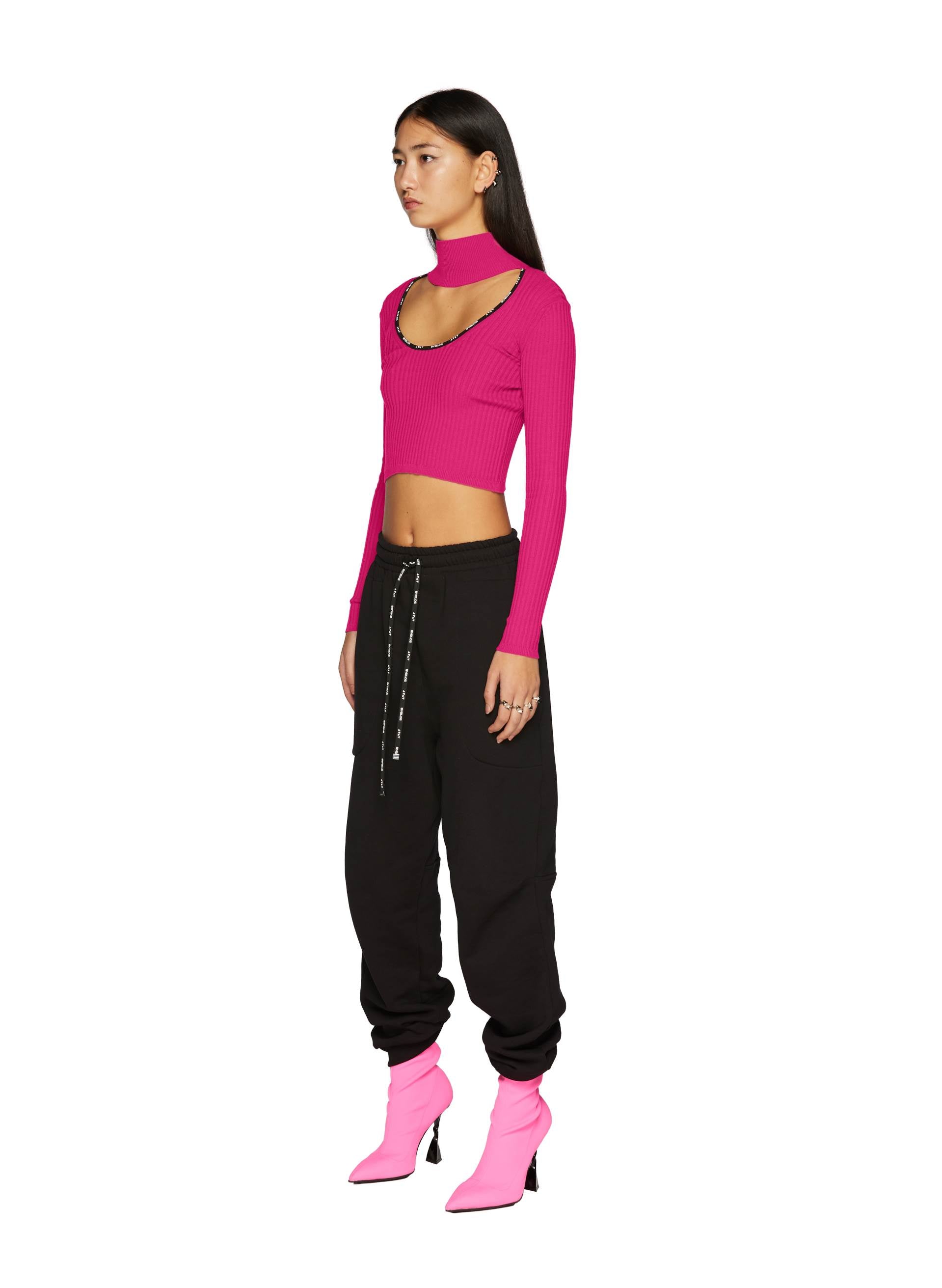 Model wearing Triangles Joggers paired with a vibrant pink Knit Logo Top Crop with a mock neck and striking pink heeled boots.