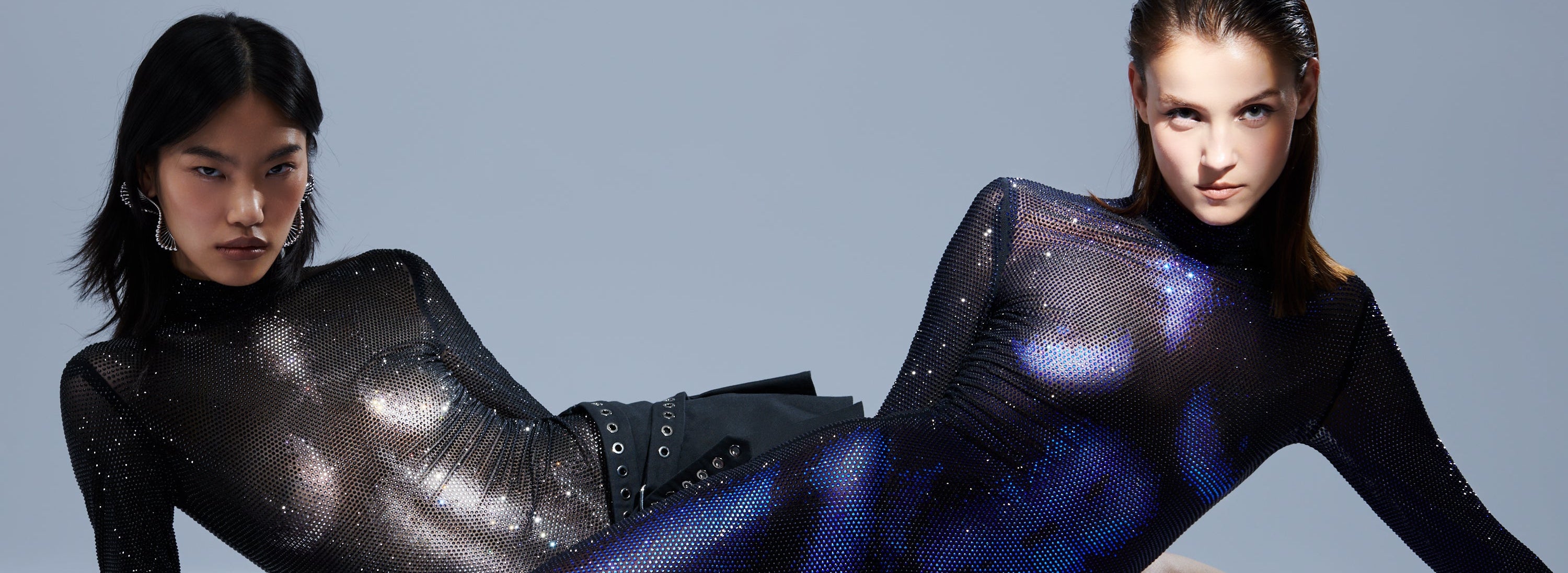 Two models wearing futuristic, reflective outfits against a gray background