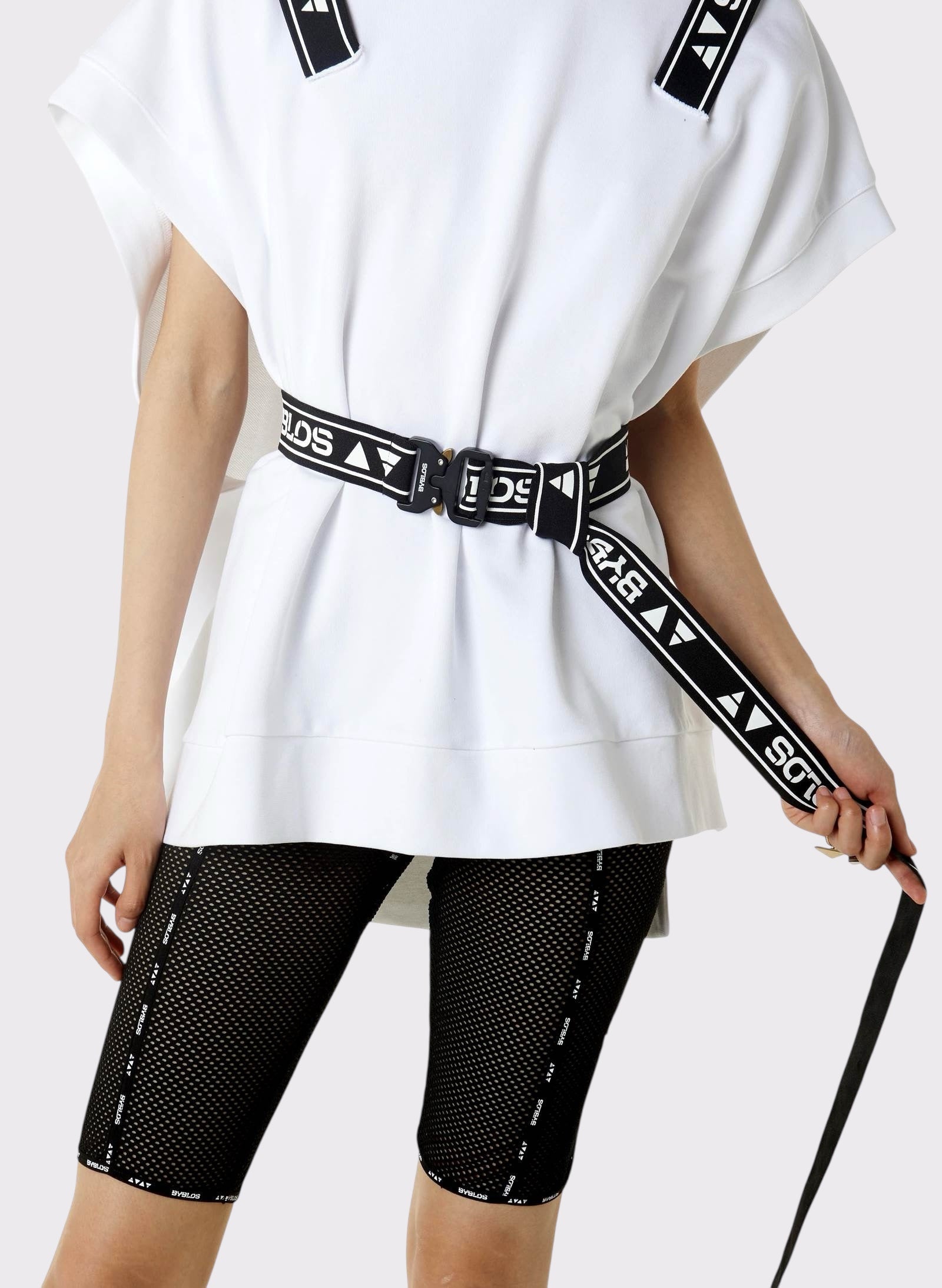 Person wearing a white oversized shirt and black shorts with a belt, on a plain background