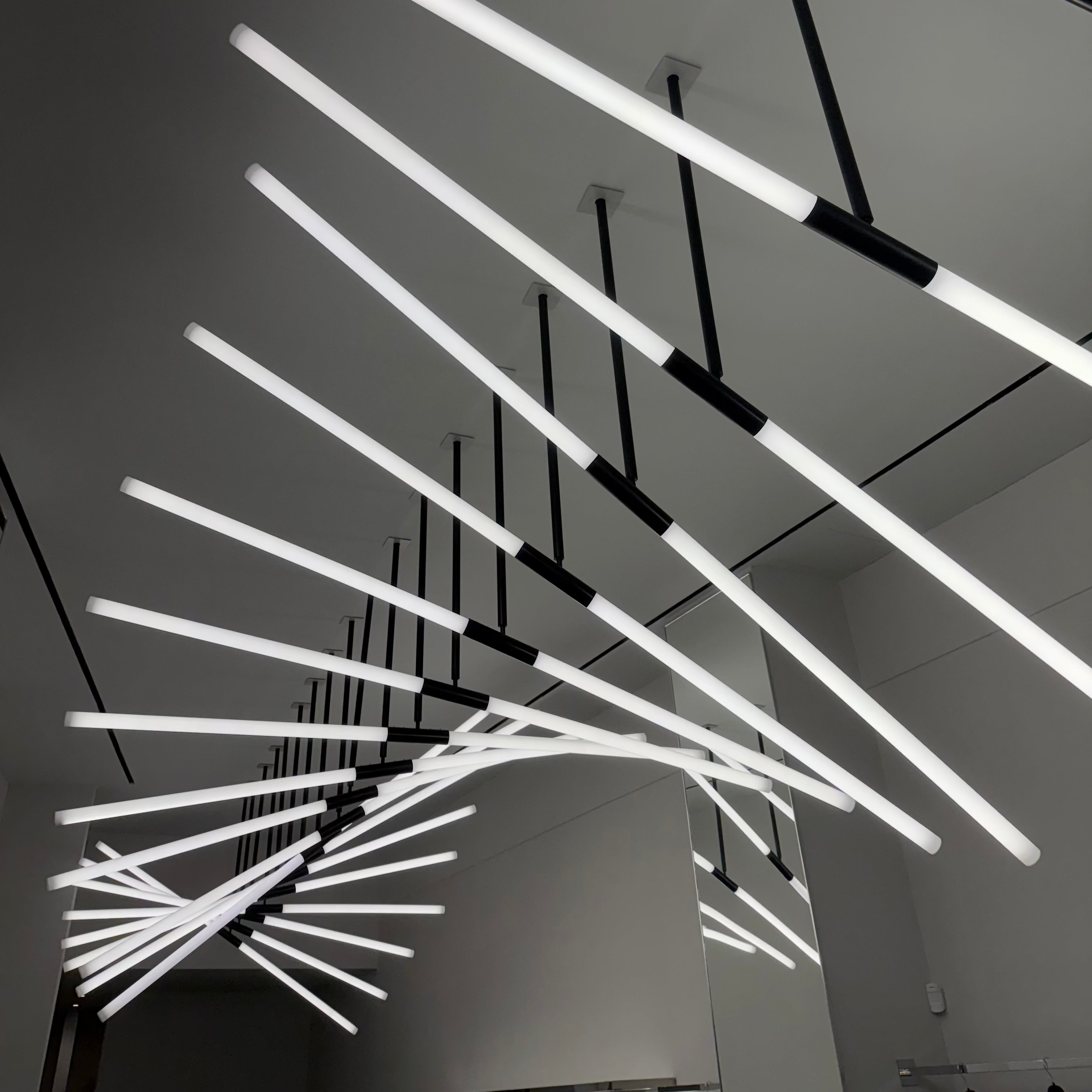 Modern ceiling light fixture with long, thin white lights on a dark ceiling.