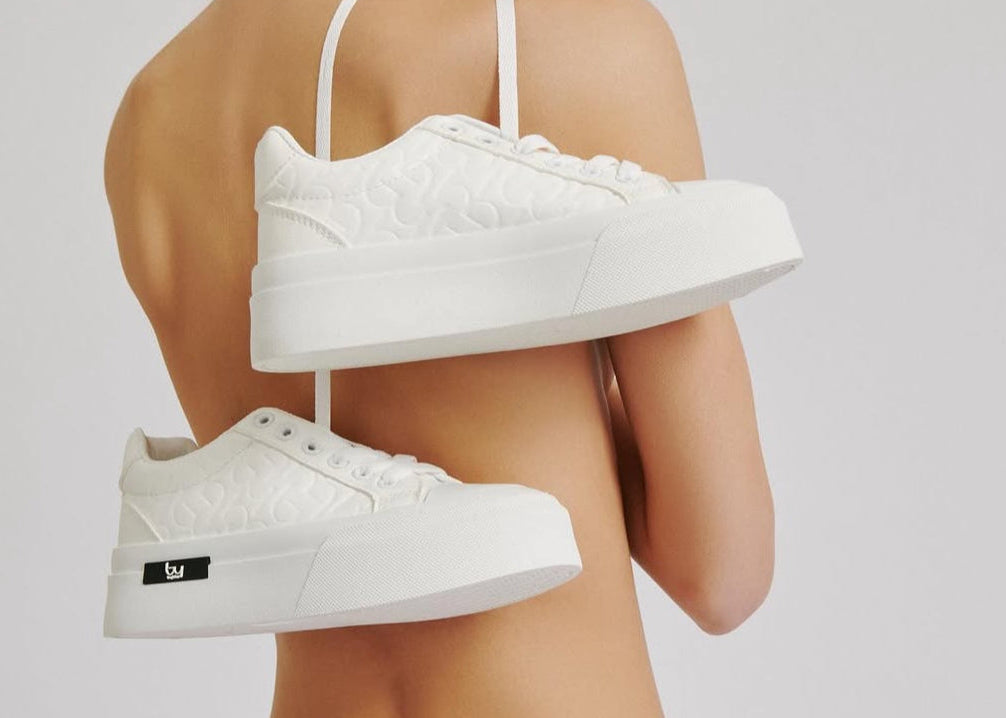 White sneakers held by a person against a plain background