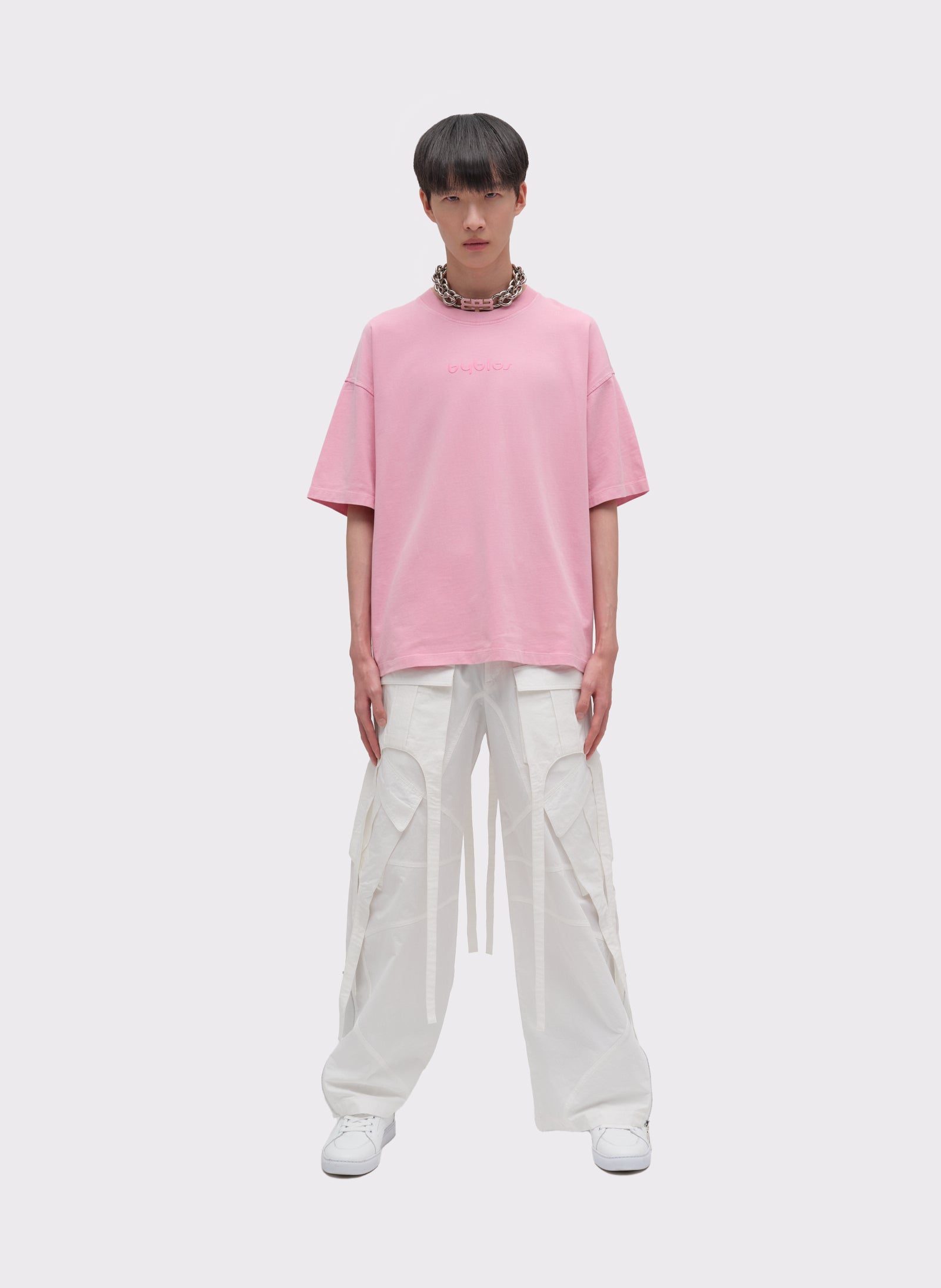 Person wearing a pink oversized t-shirt and white pants on a white background