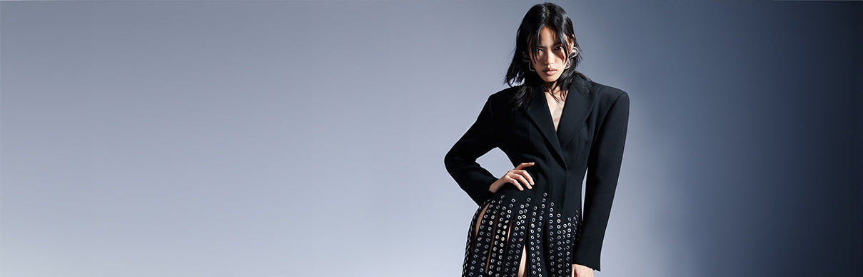 Woman wearing a black blazer over a patterned dress against a gray background