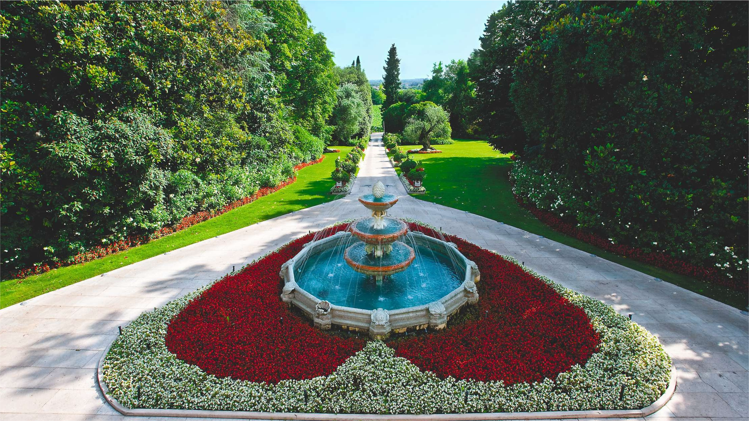 Fountain in a park with a heart-shaped flower bed and trees surrounding it