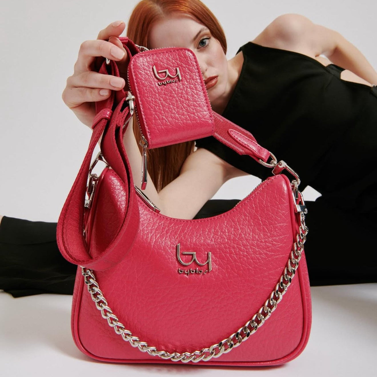 Woman holding a pink handbag with a matching wallet, both featuring a brand logo.