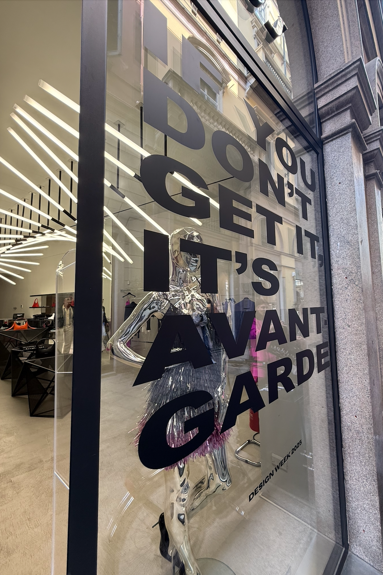 Storefront with a transparent mannequin and text on a glass door, with interior and exterior reflections.